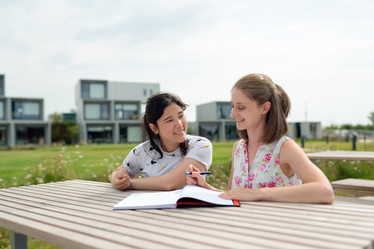 services-05 Two young women studying together outdoors on a modern campus, enjoying a sunny day.
