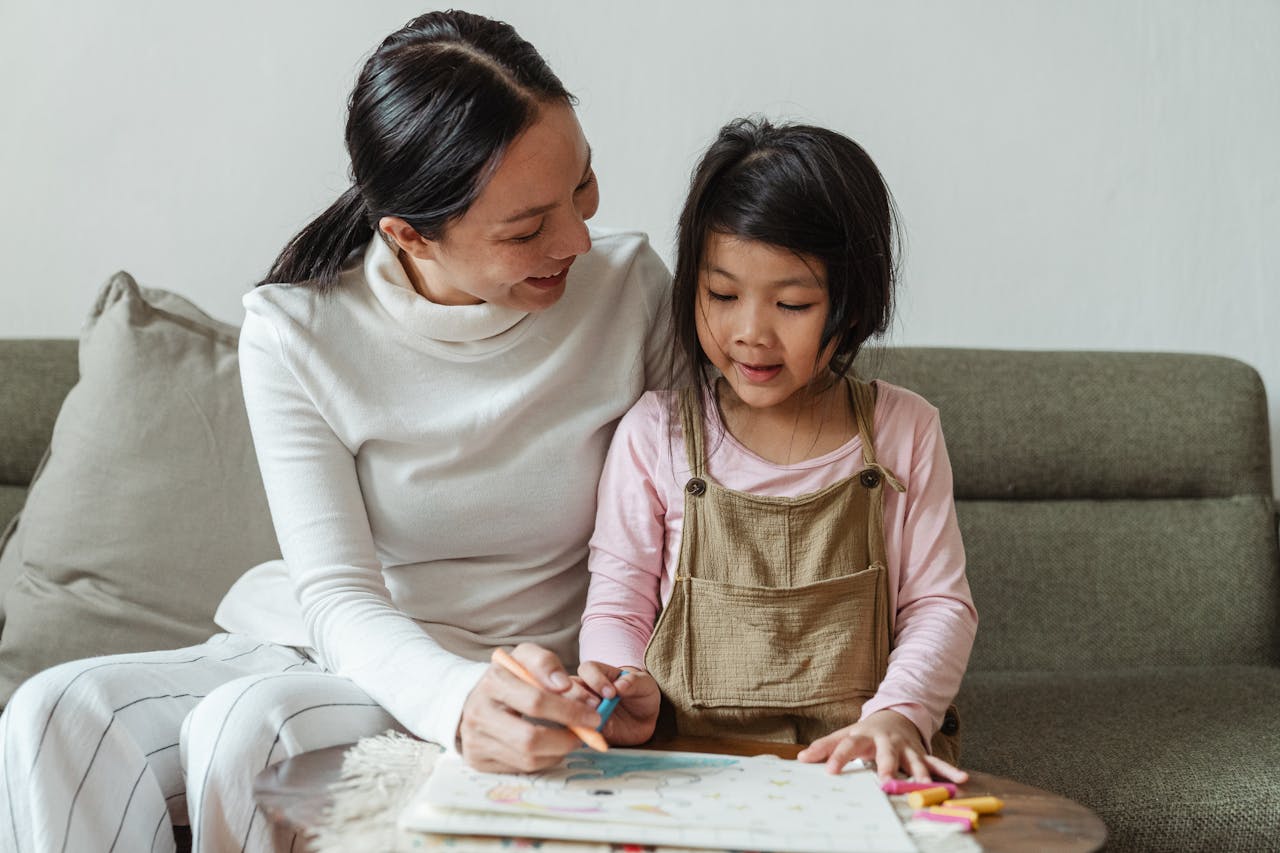 about-us A mother helps her young daughter with a colorful drawing at home, fostering creativity and bonding.