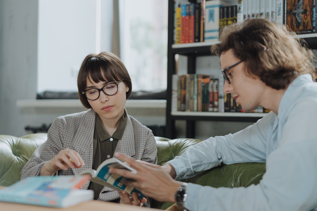 why-choose-us Two young adults reading and discussing in a cozy library space, sitting on a green sofa.
